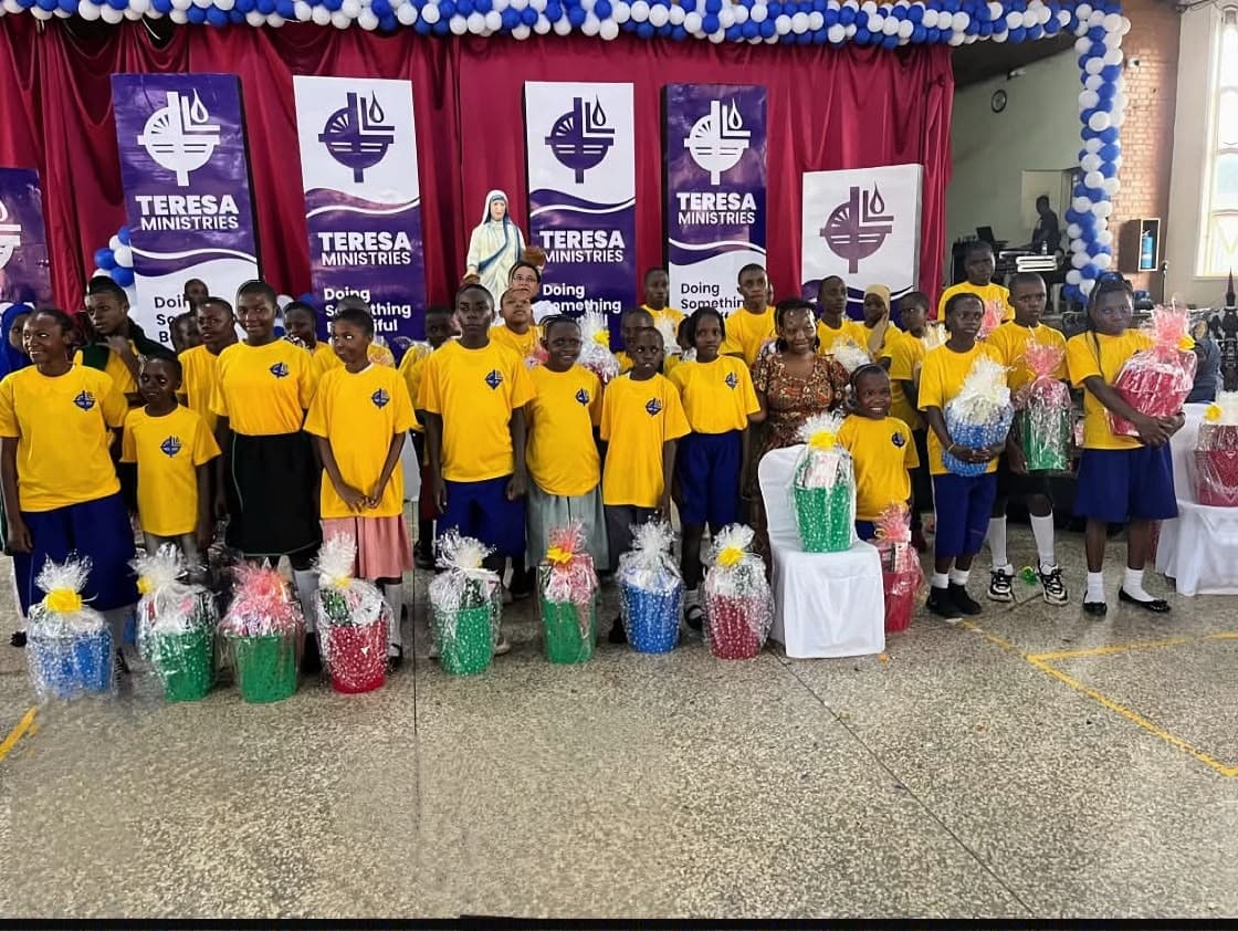 Children with gift hampers at a Teresa Ministries Uganda event beneath the ministry’s banners
